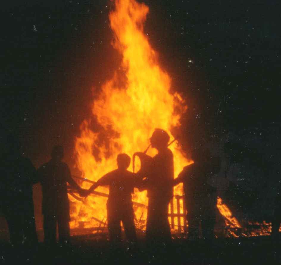 sonneur de biniou et danseurs en chaîne devant un grand feu